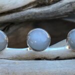 a group of silver Moonstone rings on a piece of wood