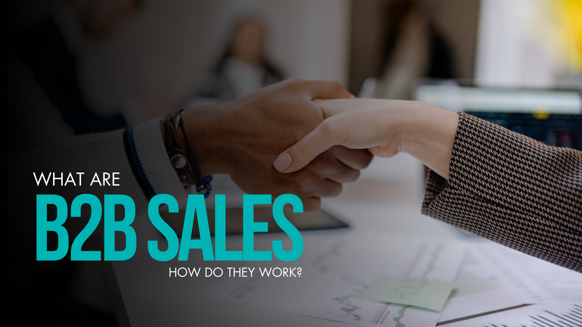 Two professionals shaking hands in a business setting, with charts, documents, and a laptop visible on the desk. Overlaid text reads, "What Are B2B Sales – How Do They Work?" highlighting a business-to-business sales concept and its operational dynamics.
