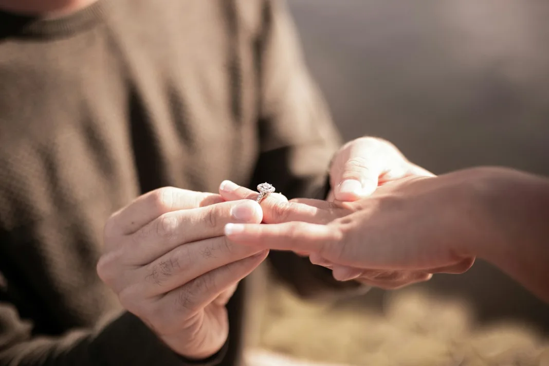 A person putting a diamond ring on a her girlfriend's finger.