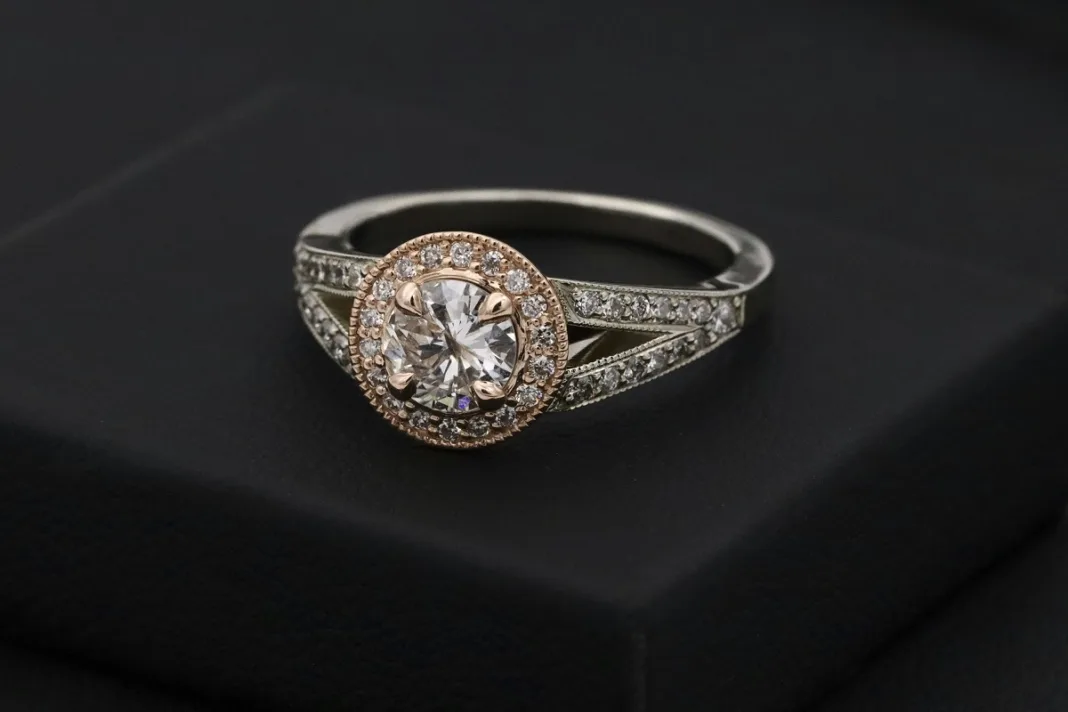 Close-up view of an elegant diamond ring featuring a round center stone surrounded by a halo of smaller diamonds, set on a split shank band with intricate diamond detailing, displayed on a black background.