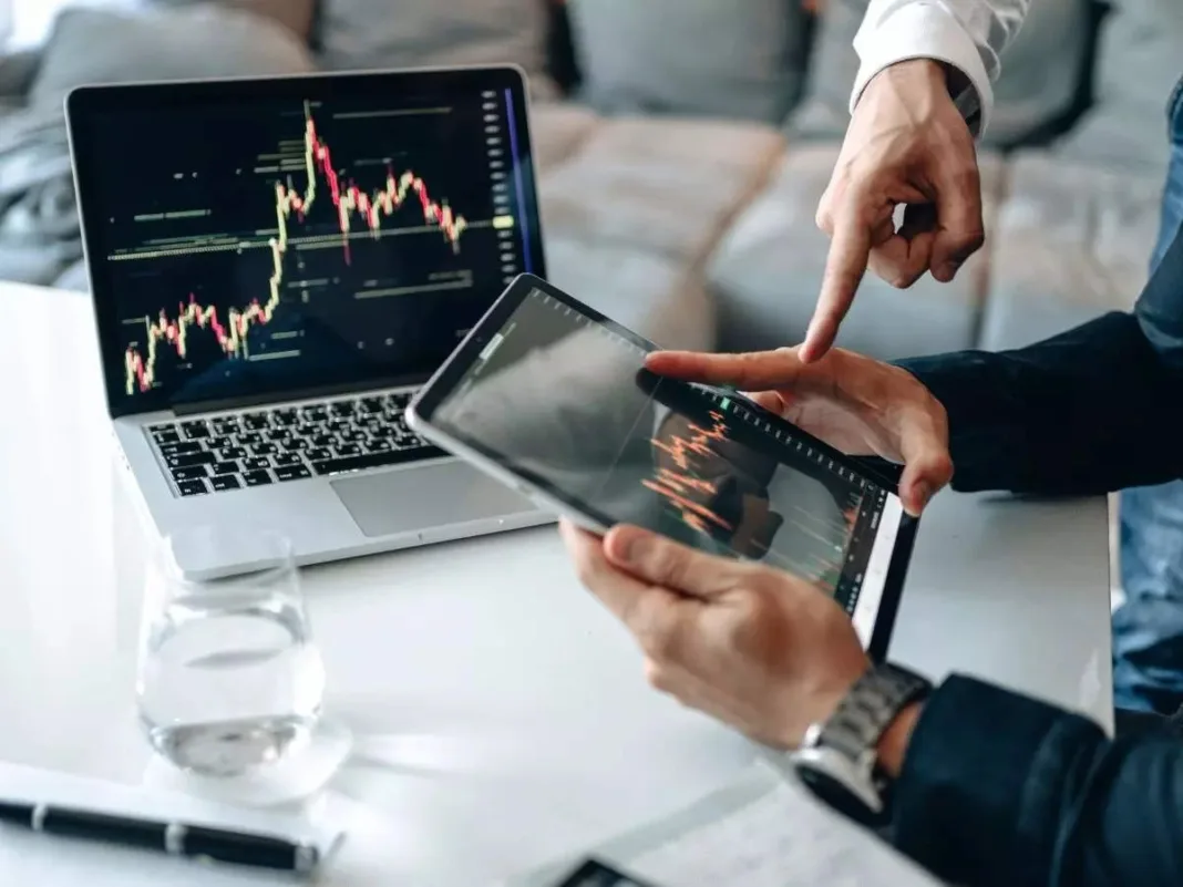 Two people analyzing stock market charts on a laptop and tablet to make smart trading decisions.